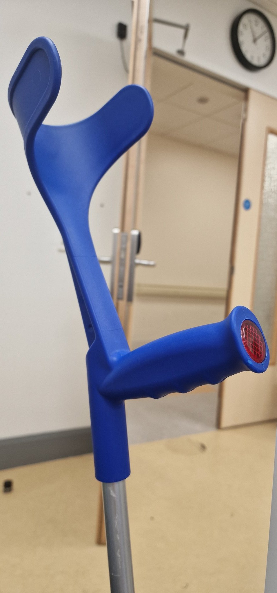 Top of a crutch with blue plastic handles and the door to a hospital waiting room
